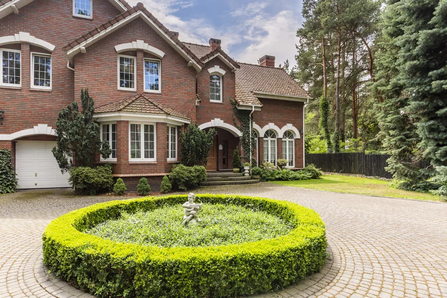 Brick house with round hedge and statue in front yard